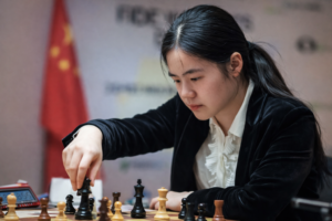 Die chinesische Schachspielerin Zhu Jiner führt während einer Partie bei einem FIDE-Turnier konzentriert einen Zug mit einer schwarzen Figur aus.