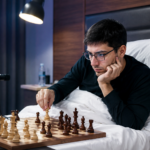 French chess player competing in a tournament while lying on a bed with a chessboard in front of him during an intense professional event.